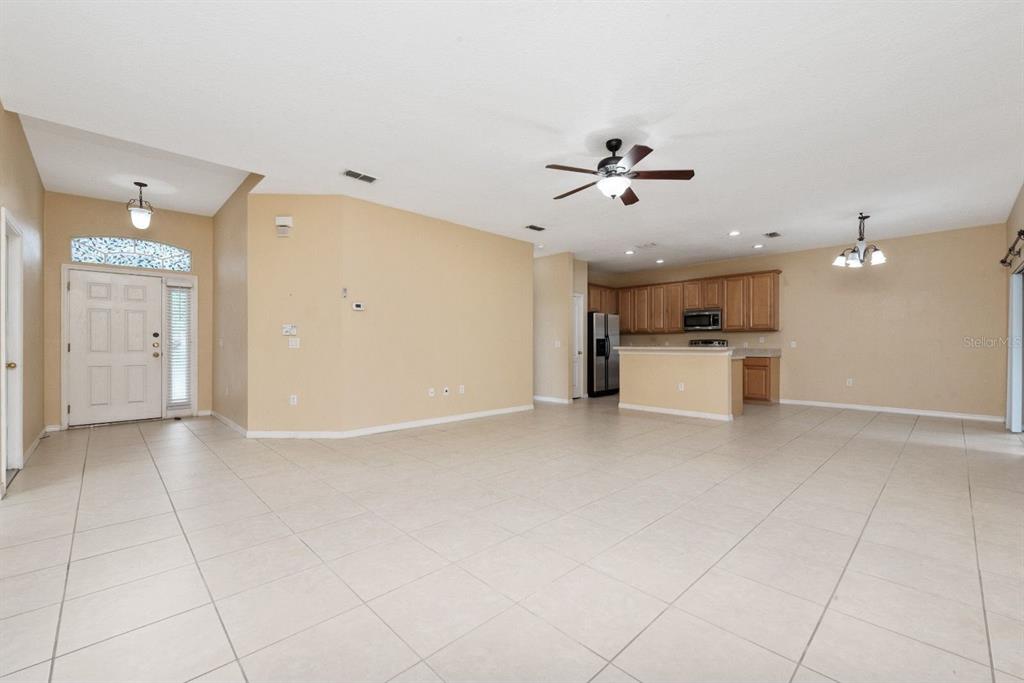 An open-concept living area features light-colored tile flooring, beige walls, and a kitchen with wood cabinets — 3857 WOOD THRUSH DRIVE, KISSIMMEE, FL