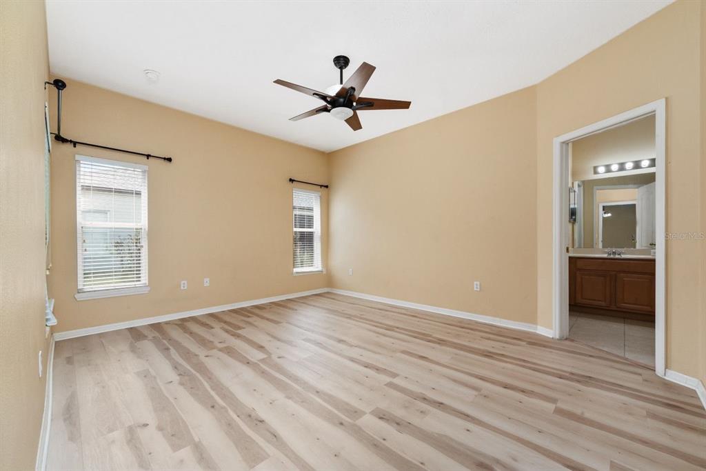 An empty bedroom with tan walls, light wood-look flooring, a ceiling fan, and an attached bathroom — 3857 WOOD THRUSH DRIVE, KISSIMMEE, FL