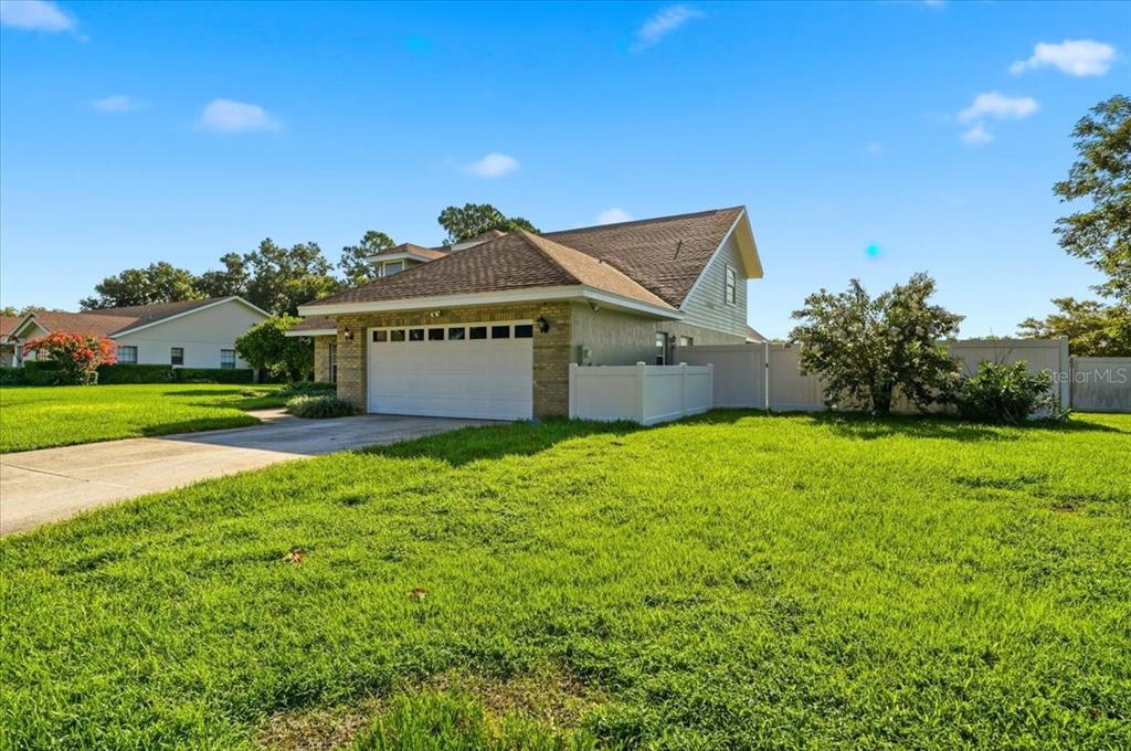 The exterior of a house features a two-car garage, a driveway, and a white fence — 814 CARLTON COURT, WINTER HAVEN, FL