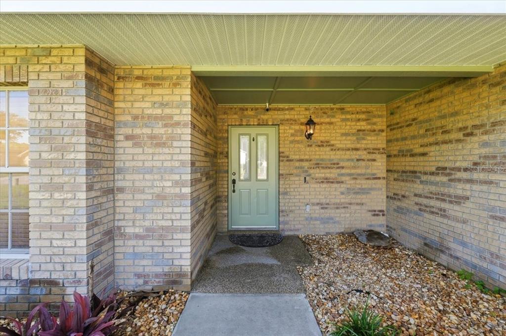 A light green front door is set within a tan brick entryway with a concrete walkway — 814 CARLTON COURT, WINTER HAVEN, FL