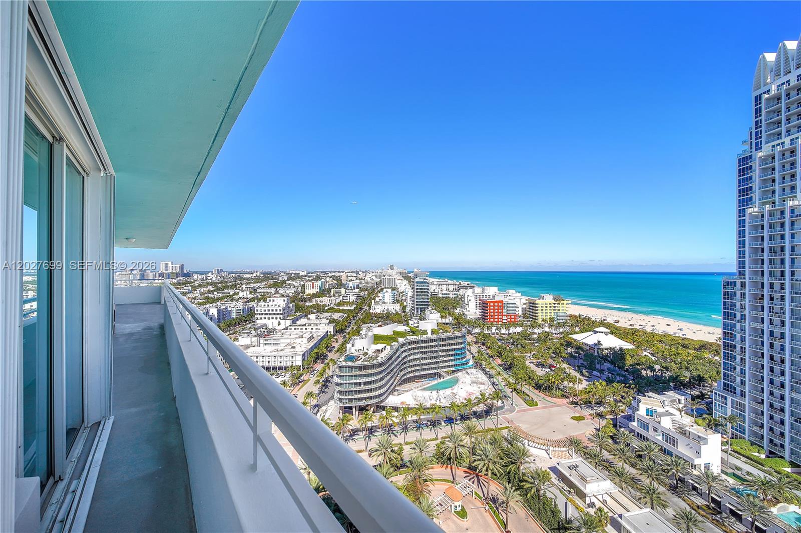 A high-rise balcony overlooks a coastal city, beach, and ocean under a clear blue sky — 400 S Pointe Dr # 2310, Miami Beach FL 33139, MIAMI BEACH, FL