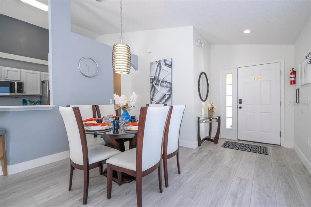 A dining area with a glass table and white chairs sits near a white front door — 2673 EMERALD ISLAND BOULEVARD, KISSIMMEE, FL