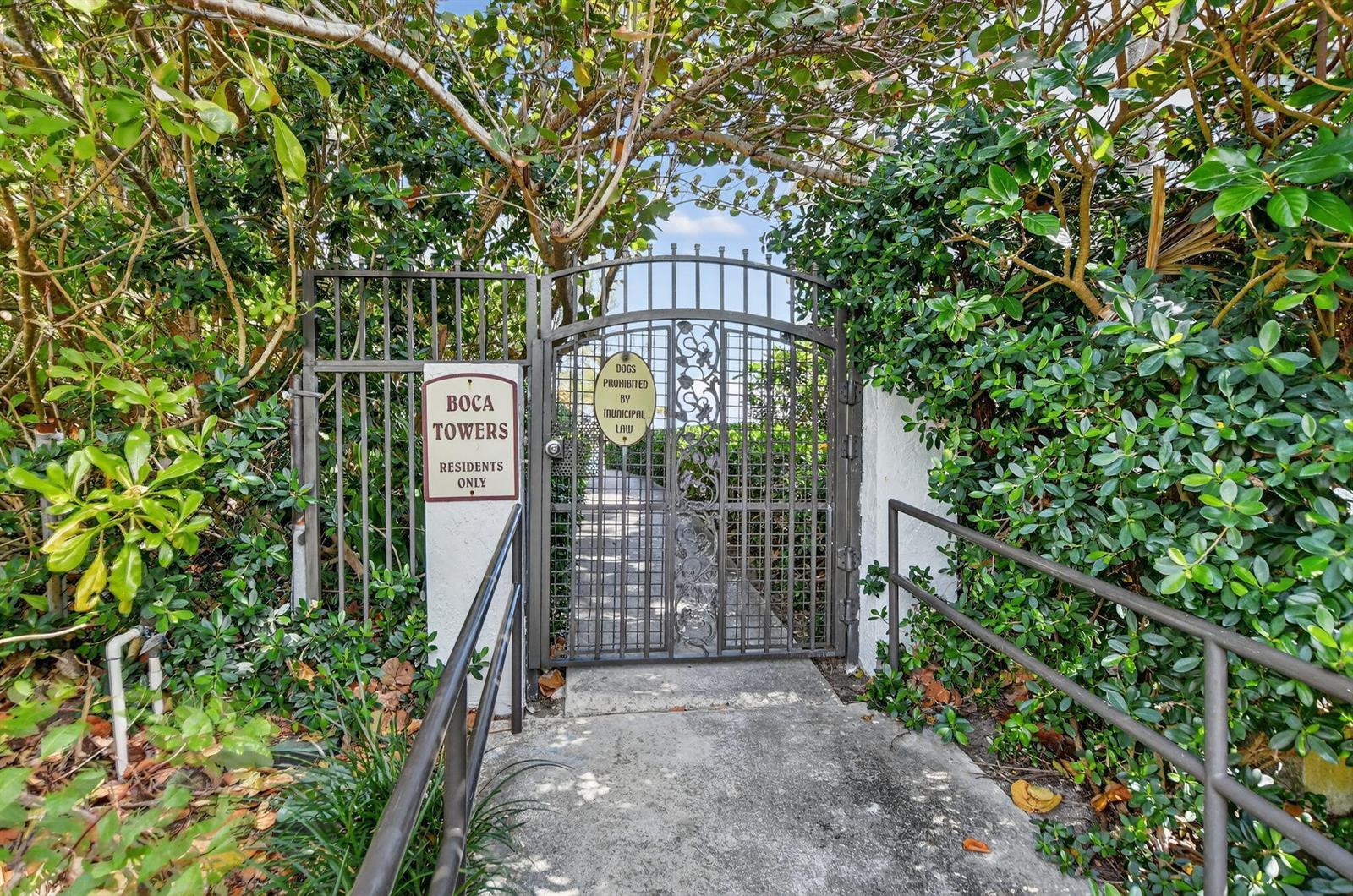 A gated entrance with a sign for Boca Towers surrounded by lush green foliage — 2121 N Ocean Boulevard # 705e, Boca Raton FL 33431, BOCA RATON, FL