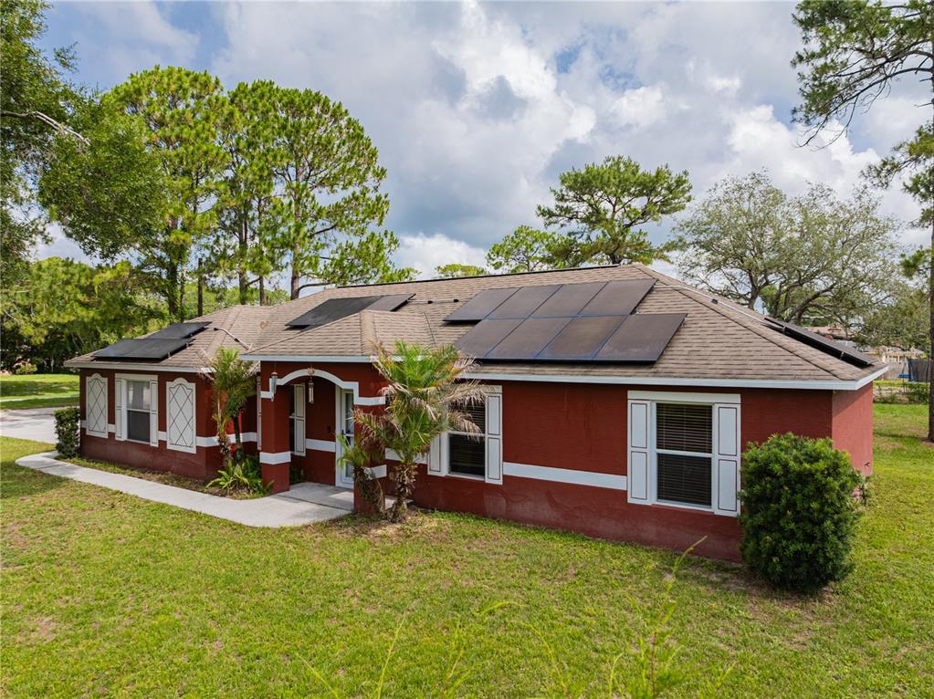 A red house with white trim and solar panels on the roof sits on a lawn — 1509 WEST PARKWAY, DELAND, FL