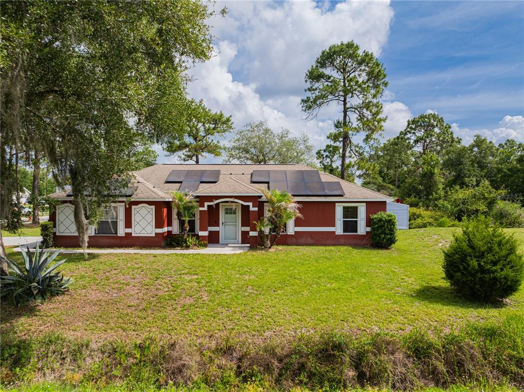 A single-story house with a red exterior, solar panels on the roof, and a front lawn — 1509 WEST PARKWAY, DELAND, FL