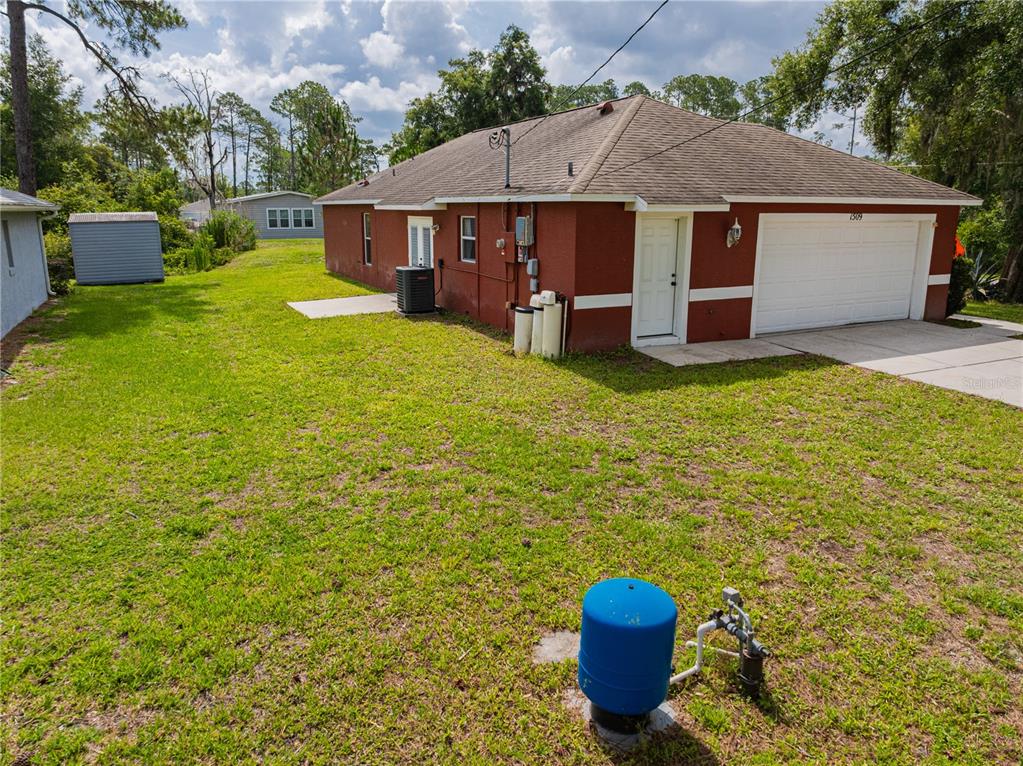 The exterior of a red house features a white garage door and a blue well tank — 1509 WEST PARKWAY, DELAND, FL