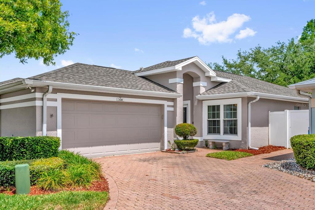 A single-story house with a beige stucco exterior, a two-car garage, and a brick driveway — 3440 GRENVILLE DRIVE, WINTER HAVEN, FL