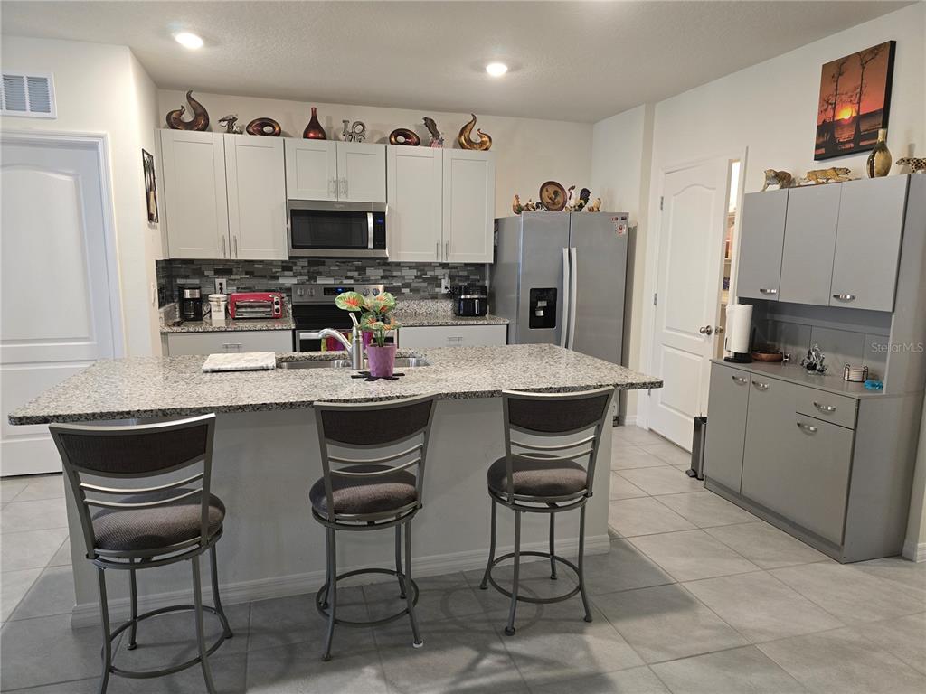 A kitchen features white upper cabinets, a granite island with bar stools, and grey cabinetry — 532 EMILY GLEN STREET, DELAND, FL