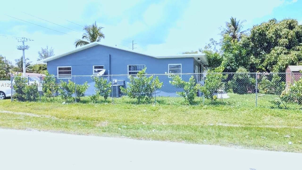 A blue single-story house is viewed from behind a chain-link fence on a grassy lot — 14615 NE 14th Ave, Miami FL 33161, MIAMI, FL