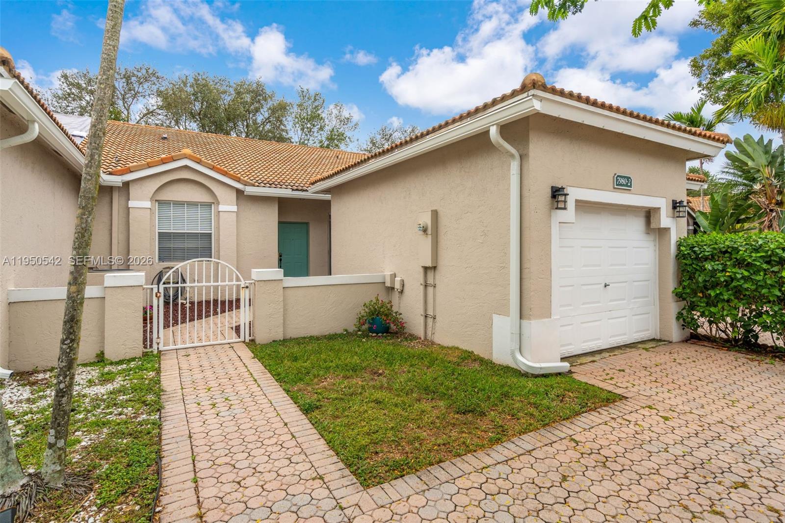 The exterior of a beige stucco house features a tiled roof, garage, and gated courtyard — 7980 S Aragon Blvd # 2, Sunrise FL 33322, SUNRISE, FL