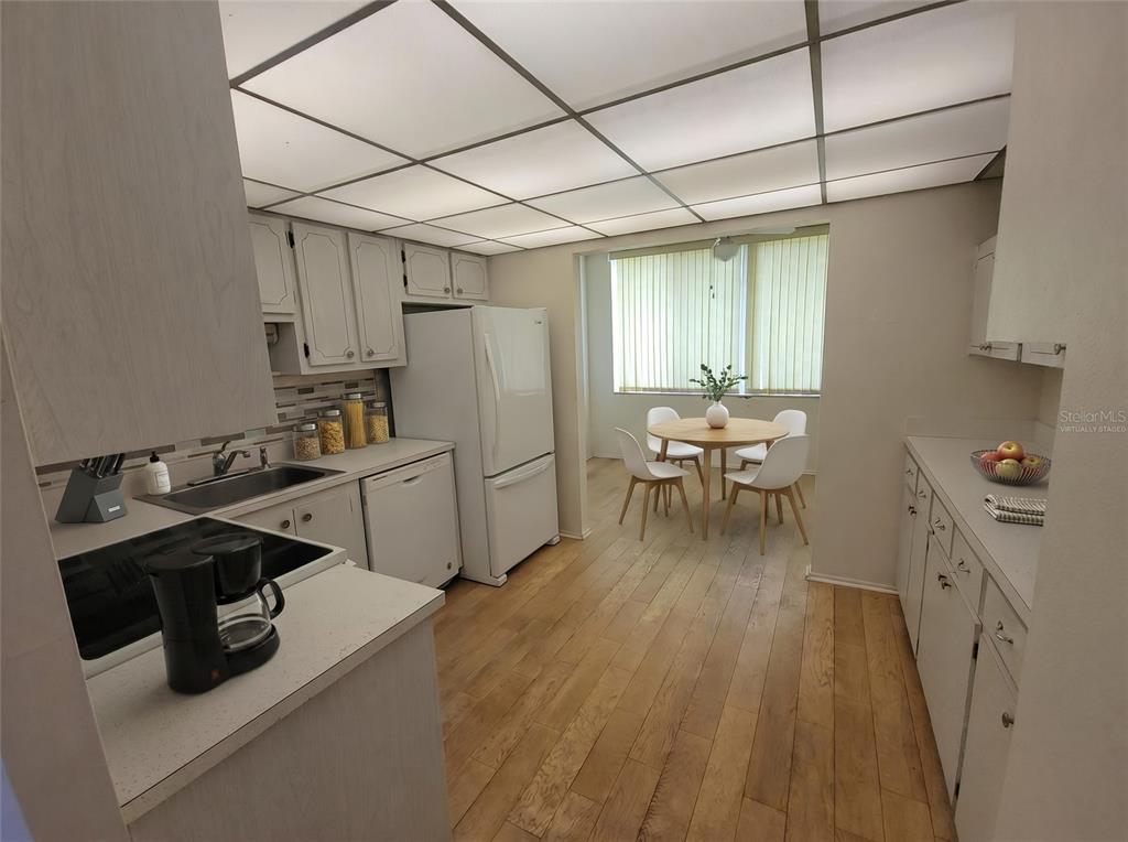 A kitchen features white cabinetry, a drop ceiling, wood-look flooring, and an adjacent dining area — 4890 BAY STREET NE UNIT 336, ST PETERSBURG, FL