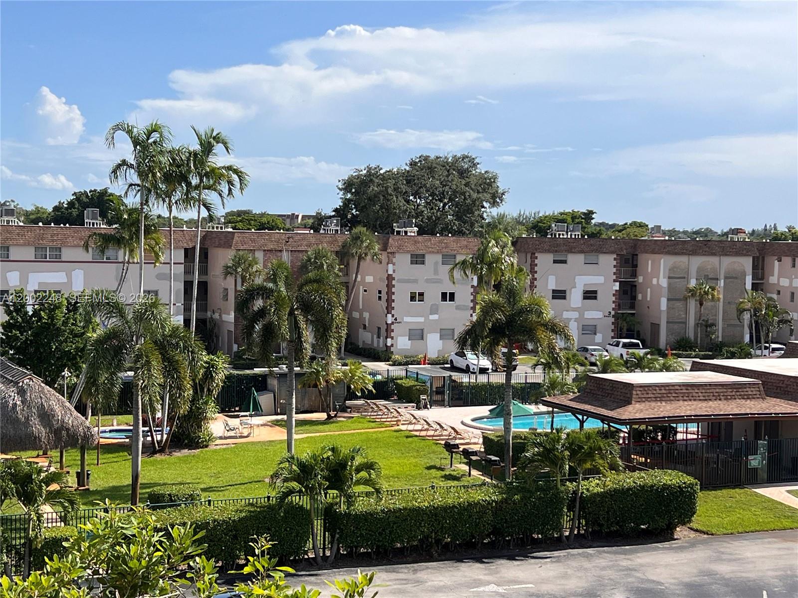 An exterior view of a multi-story apartment complex with a swimming pool and palm trees — 8101 SW 24th Ct # 406, Davie FL 33324, DAVIE, FL