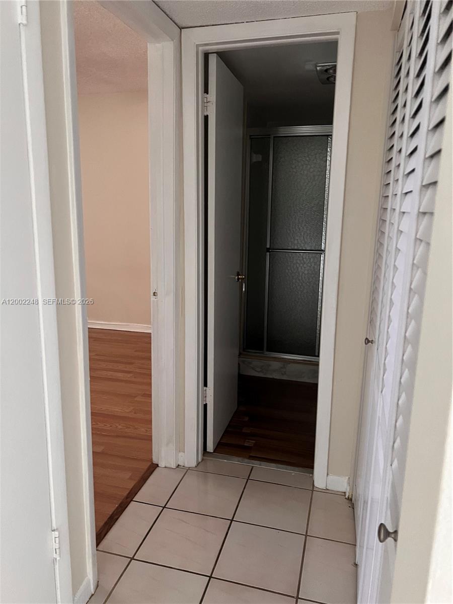A hallway with tiled flooring leads to a bathroom with a glass-enclosed shower — 8101 SW 24th Ct # 406, Davie FL 33324, DAVIE, FL