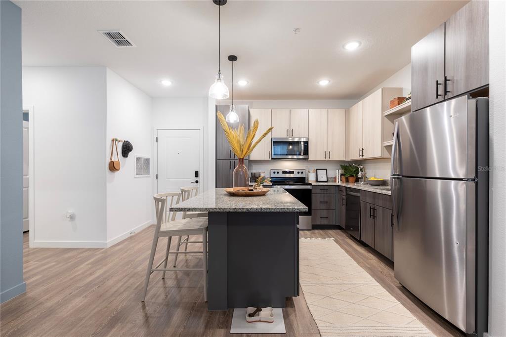 A modern kitchen features a dark gray island, stainless steel appliances, and light wood cabinetry — 10105 SELTEN WAY, ORLANDO, FL