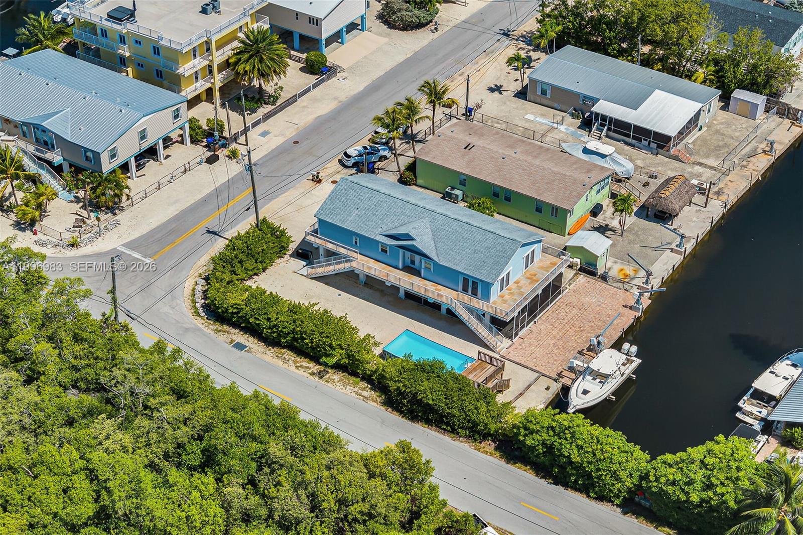A light blue stilt house sits beside a canal with a boat on a lift — 103 Long Key Rd, Key Largo FL 33037, KEY LARGO, FL