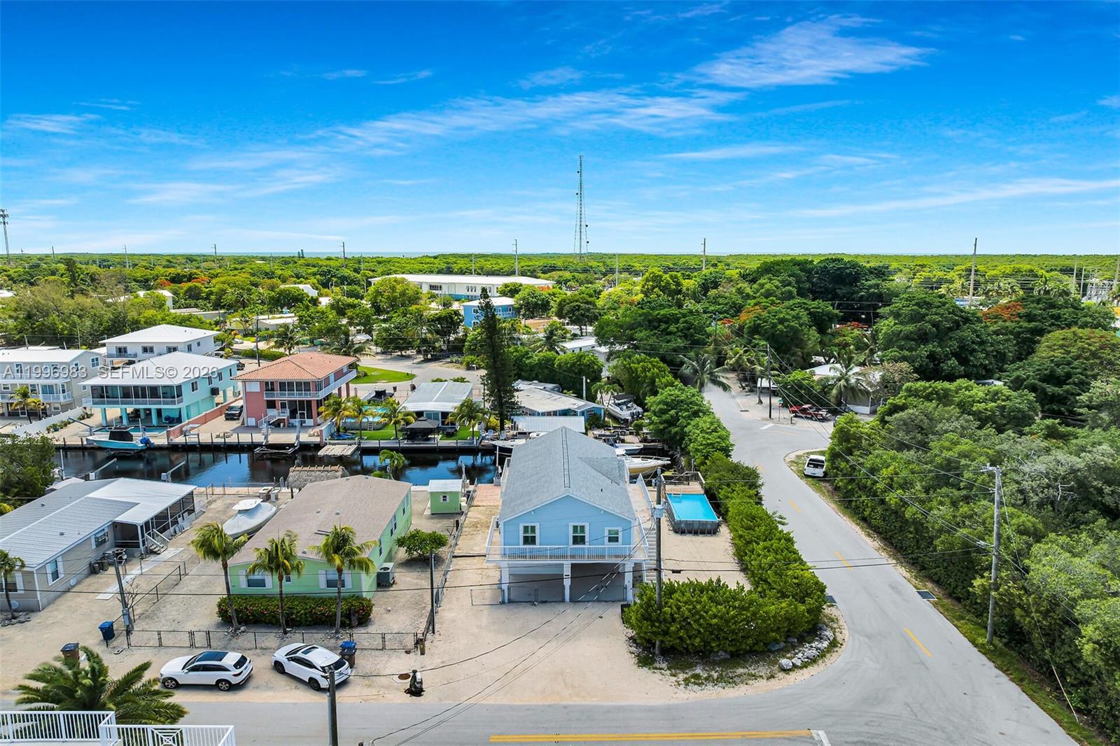 An elevated light blue house features a large deck, white railings, and a paved patio — 103 Long Key Rd, Key Largo FL 33037, KEY LARGO, FL