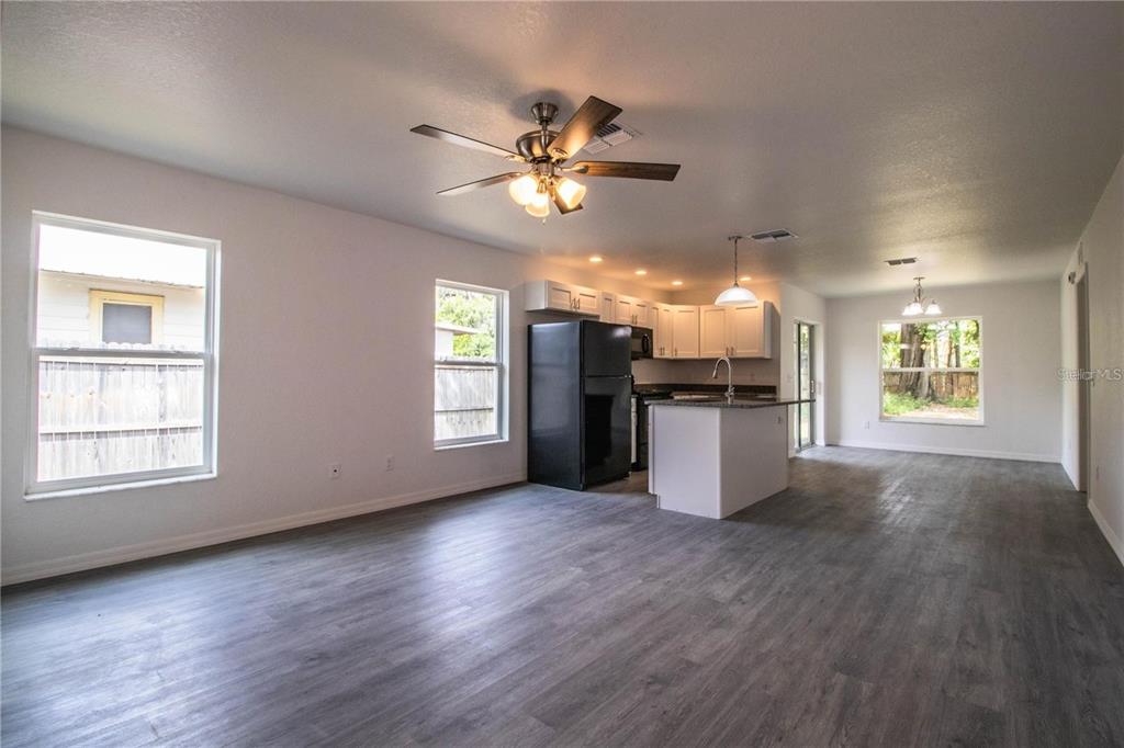 An open-concept living area features gray wood-look flooring, a ceiling fan, and a kitchen — 1437 AMOS AVENUE, LAKELAND, FL
