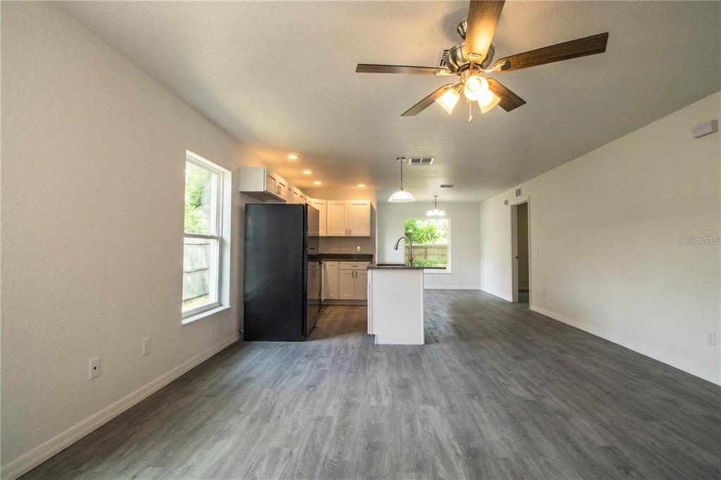An open-concept kitchen and living area featuring gray wood-look flooring and a black refrigerator — 1437 AMOS AVENUE, LAKELAND, FL