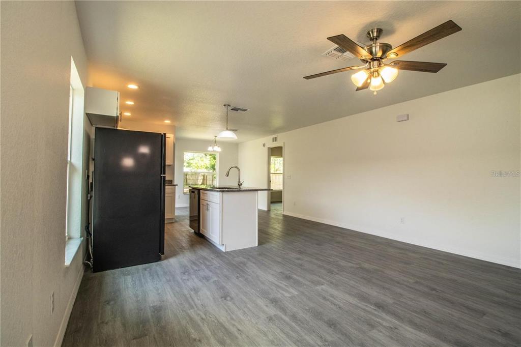 An open-concept kitchen and living area features gray wood-look flooring and white cabinetry — 1437 AMOS AVENUE, LAKELAND, FL
