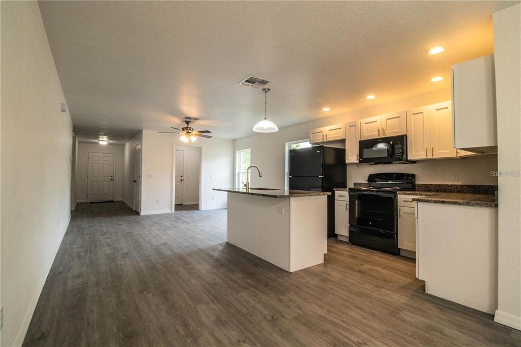 An open-concept kitchen features white cabinets, granite countertops, and black appliances over wood-look flooring — 1437 AMOS AVENUE, LAKELAND, FL