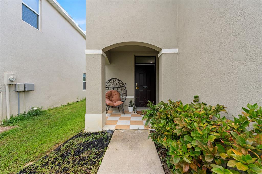 A covered entryway features a checkered tile floor, a hanging chair, and a dark door — 10828 TRAILING VINE DRIVE, TAMPA, FL