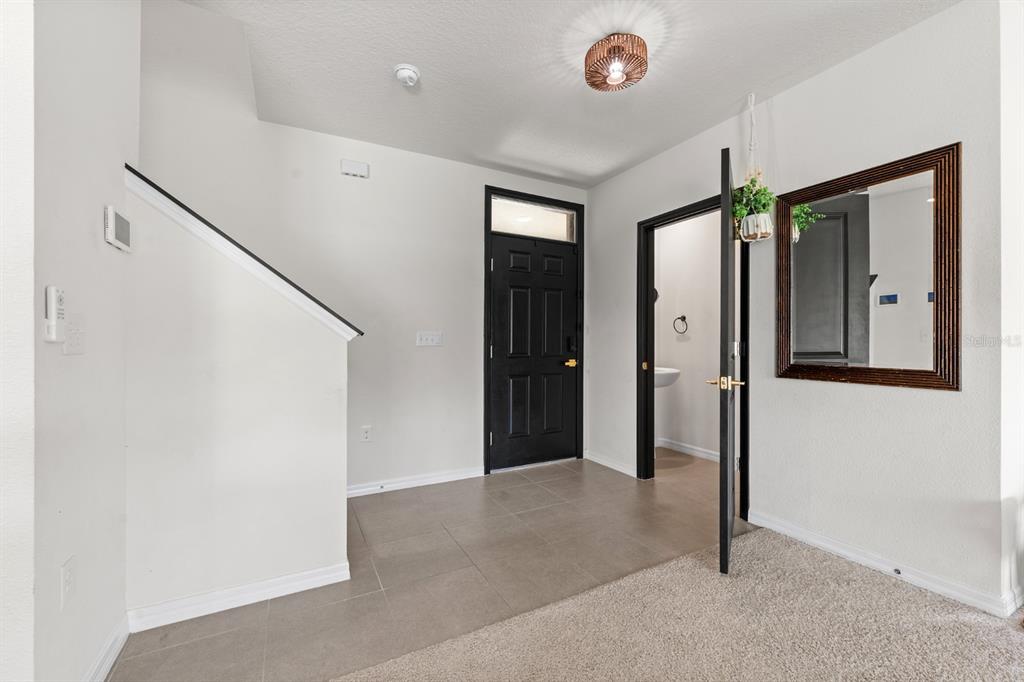 An entryway features tile flooring, a black front door, a half bathroom, and a mirror — 10828 TRAILING VINE DRIVE, TAMPA, FL