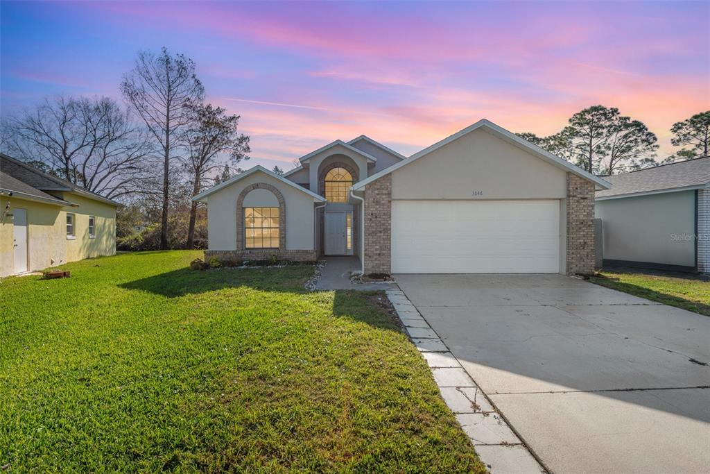 A single-story house with a white garage, brick accents, and a front lawn at sunset — 3846 LONG GROVE LANE, PORT ORANGE, FL