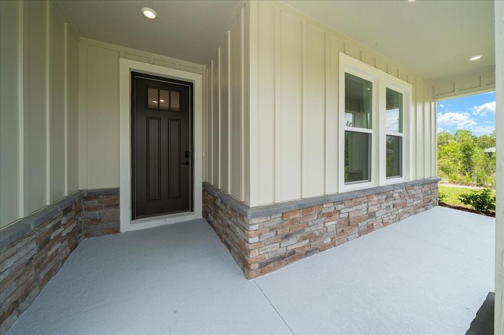 A covered front porch features light-colored vertical siding, stone veneer accents, and a dark front door — 16213 PENN STATE ROAD, WEEKI WACHEE, FL