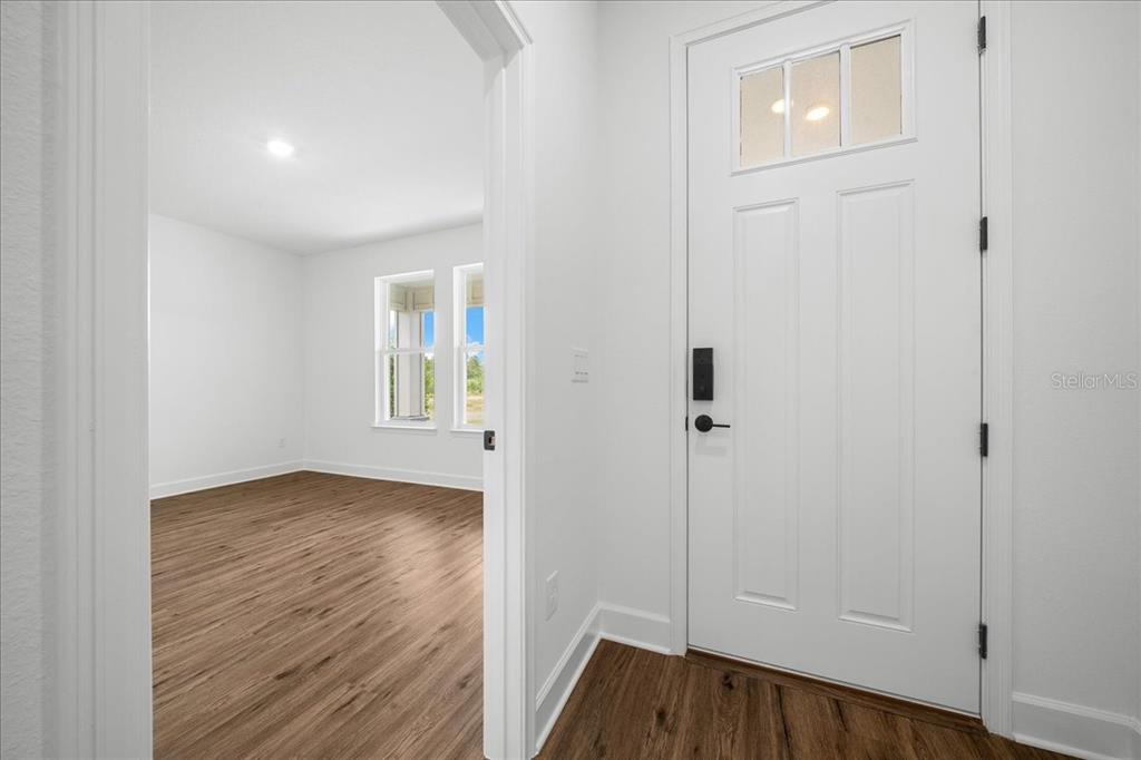 A white front door opens into a room with light wood-look flooring and white walls — 16213 PENN STATE ROAD, WEEKI WACHEE, FL