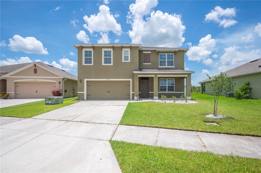 A two-story suburban house with a tan stucco exterior, a two-car garage, and a lawn — 2062 BLUE HIGHLANDS DRIVE, LAKELAND, FL