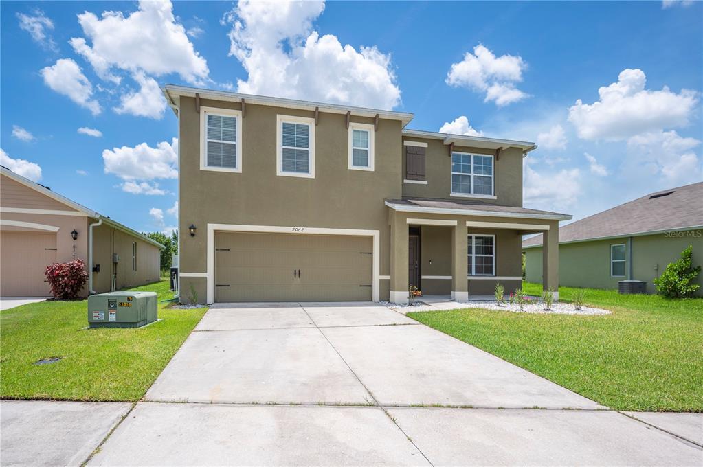 A two-story house with a tan stucco exterior, a two-car garage, and a concrete driveway — 2062 BLUE HIGHLANDS DRIVE, LAKELAND, FL
