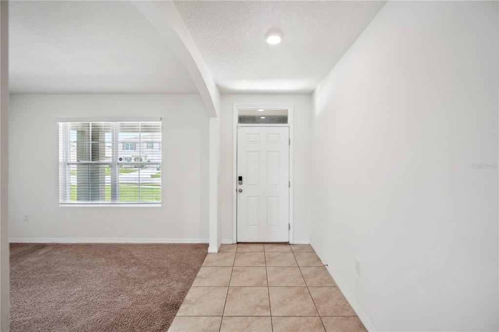 An entryway with tile flooring leads to a white front door next to a carpeted room — 2062 BLUE HIGHLANDS DRIVE, LAKELAND, FL