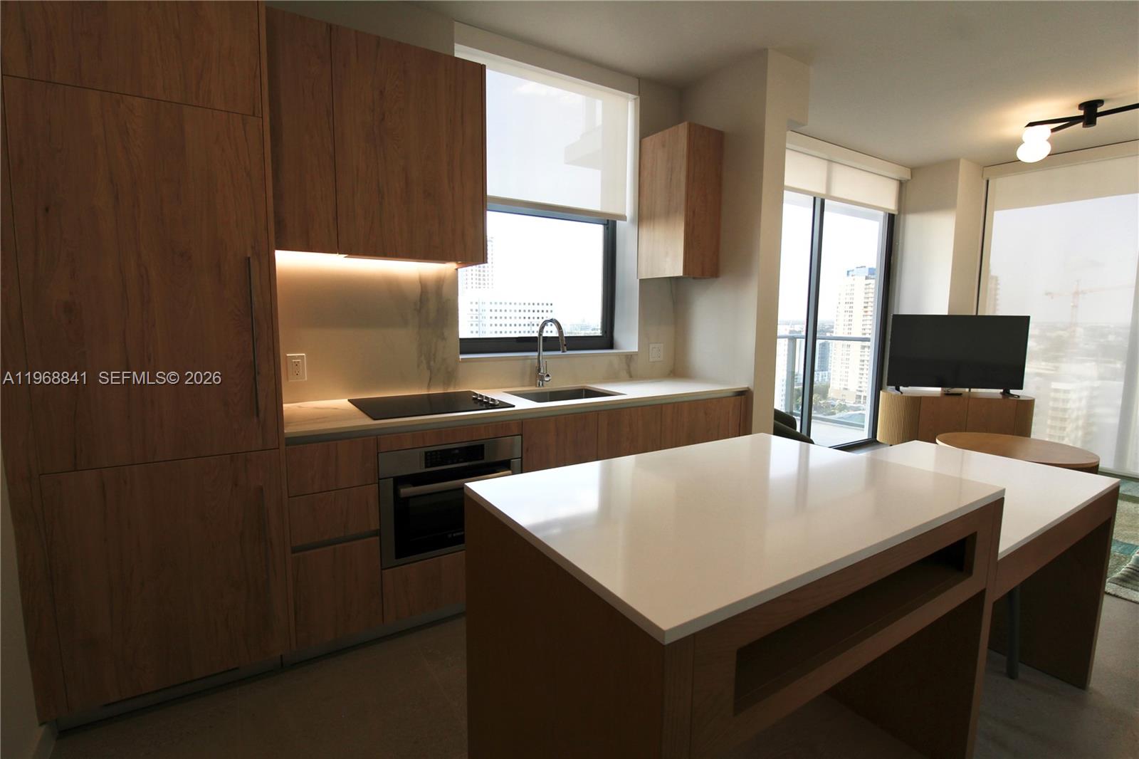A modern kitchen features wood-toned cabinetry, white countertops, and an island with a dining extension — 11 NE 6 St # 2114, Miami FL 33132, MIAMI, FL