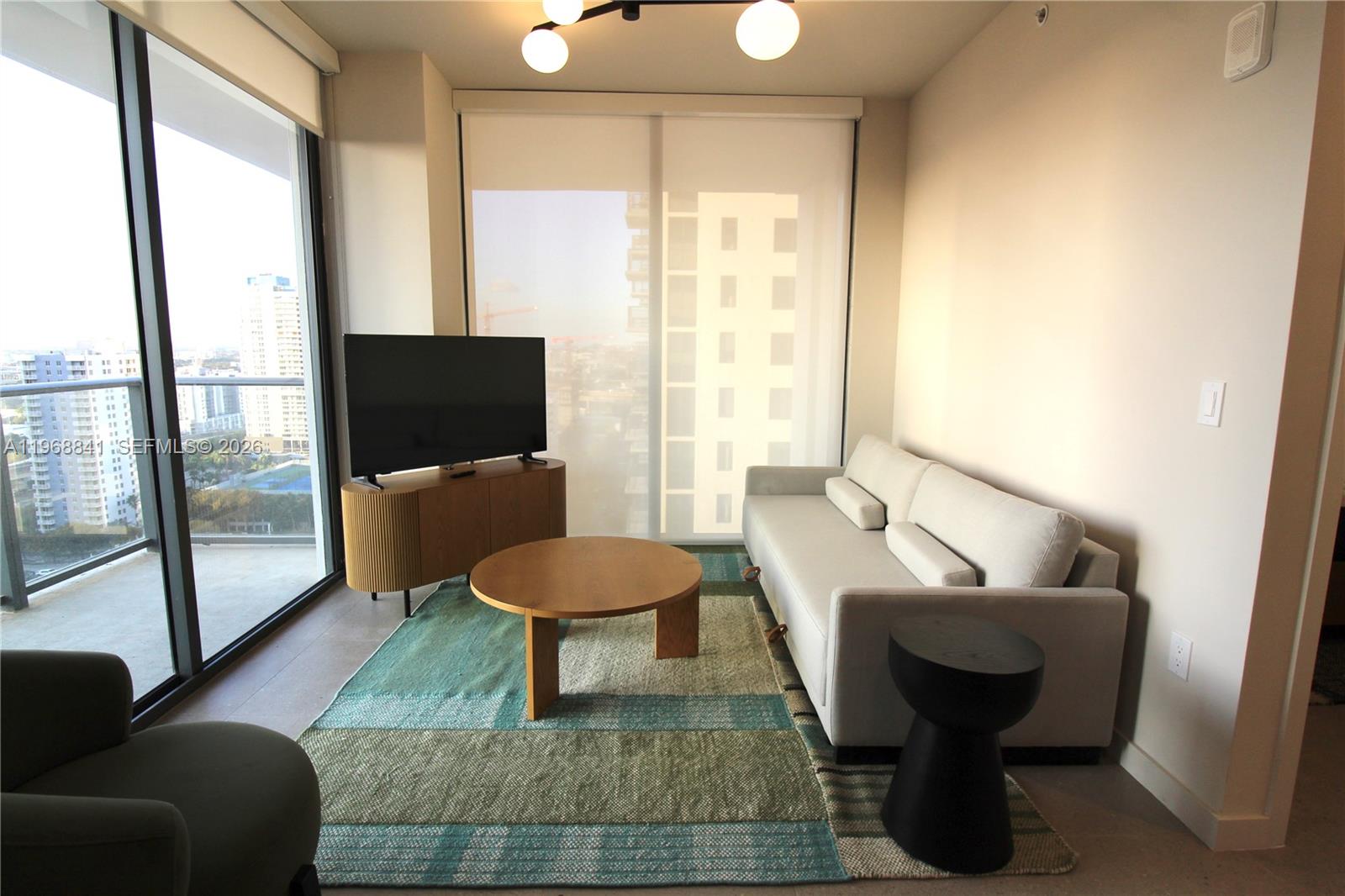 A living room features a light-colored sofa, a round wooden coffee table, and floor-to-ceiling windows — 11 NE 6 St # 2114, Miami FL 33132, MIAMI, FL