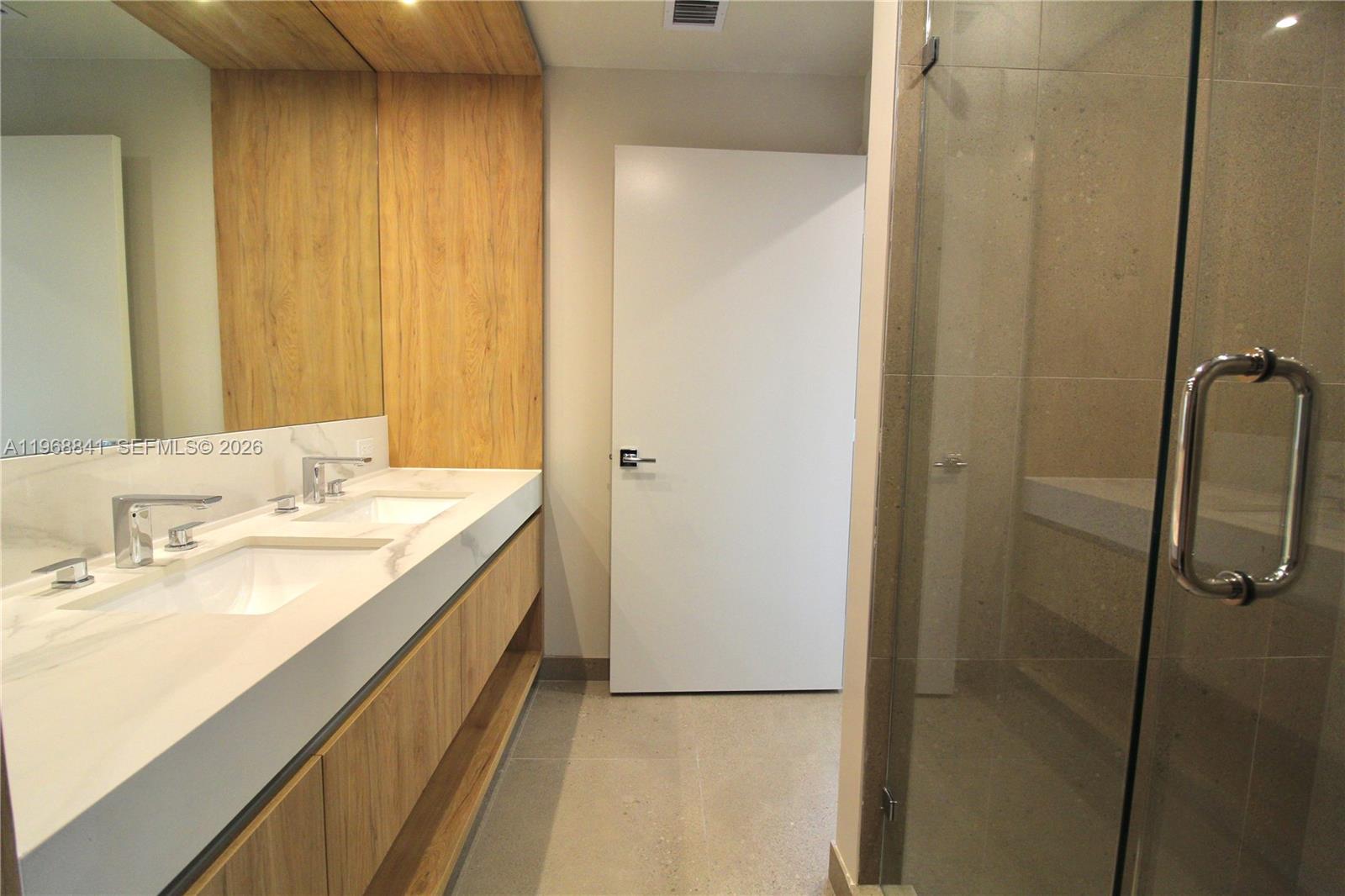 A modern bathroom features a double vanity with wood cabinetry and a glass-enclosed shower — 11 NE 6 St # 2114, Miami FL 33132, MIAMI, FL