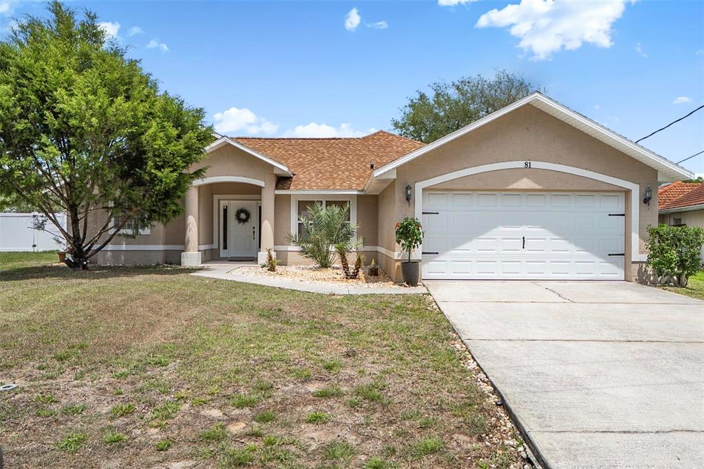 A single-story house with a tan stucco exterior, brown shingled roof, and a two-car garage — 81 FREEMONT TURN, PALM COAST, FL