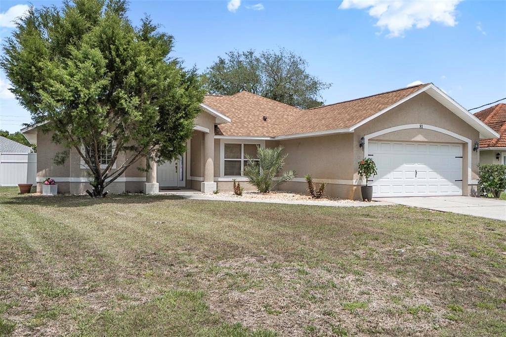 A single-story tan stucco house features a two-car garage and a large front yard tree — 81 FREEMONT TURN, PALM COAST, FL