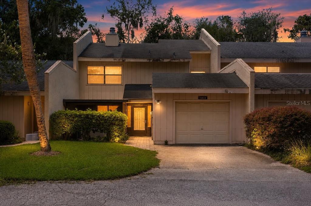 A two-story townhouse with a beige exterior, a single-car garage, and a paved walkway — 11418 PALMETTO BOULEVARD, ALACHUA, FL