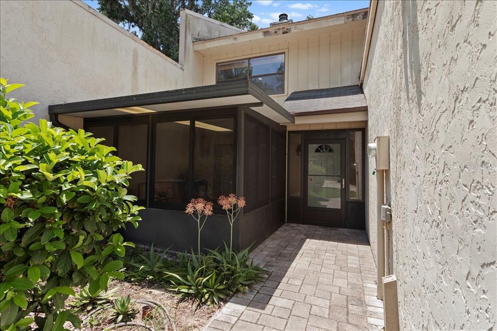 A paved walkway leads to a front entrance beside a screened-in porch and stucco walls — 11418 PALMETTO BOULEVARD, ALACHUA, FL