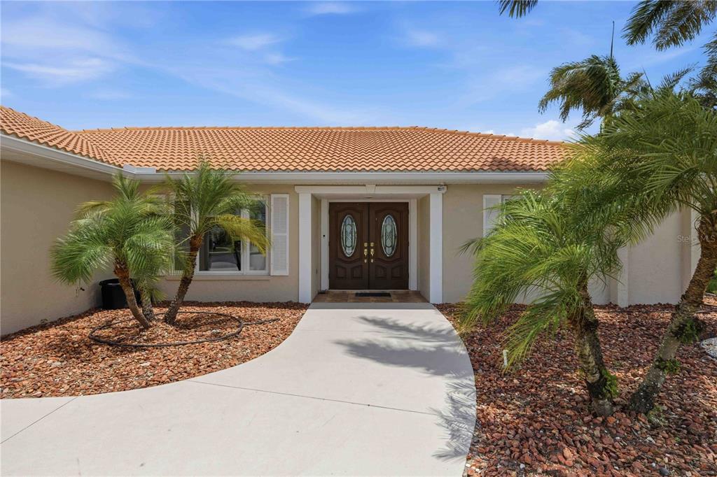 A beige house exterior features a double front door, a tiled roof, and palm trees — 1714 CLAW COURT, VENICE, FL