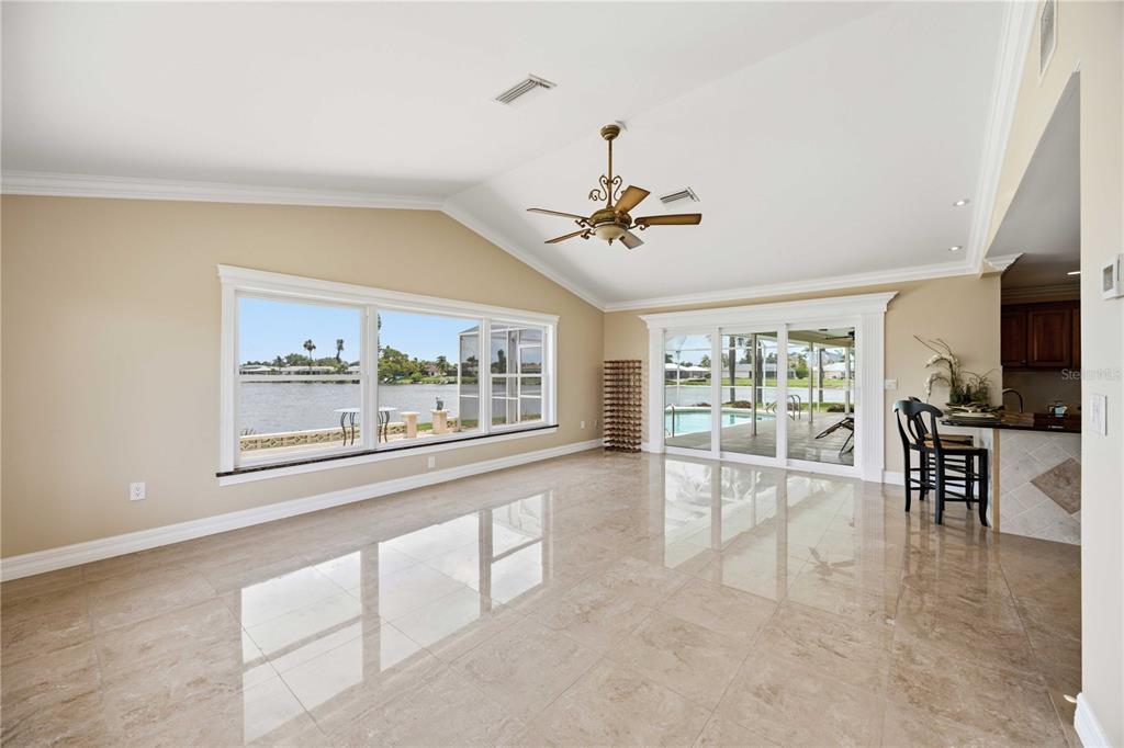 A spacious living room features beige tile floors, a vaulted ceiling, and large waterfront windows — 1714 CLAW COURT, VENICE, FL