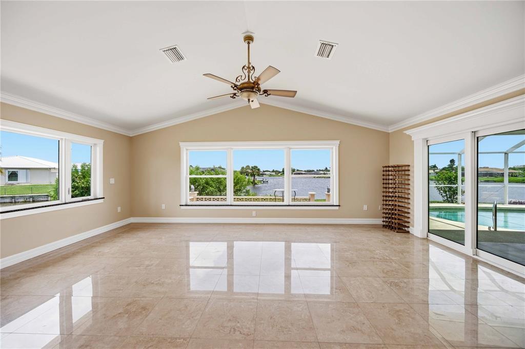 A spacious, empty room with beige tile floors, a vaulted ceiling, and large windows overlooking water — 1714 CLAW COURT, VENICE, FL
