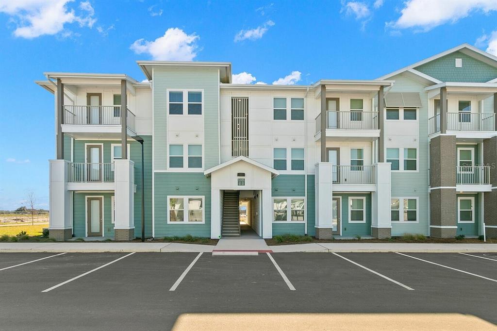 A three-story apartment building with light green and white siding stands behind a parking lot — 5476 ANGEL WAY UNIT A1, ST CLOUD, FL
