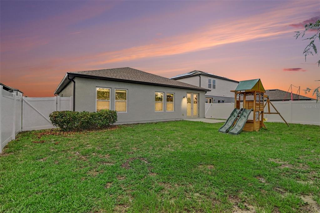 The backyard of a single-story house features a lawn, a playset, and white vinyl fencing — 1034 ALABASTER WAY, DELTONA, FL