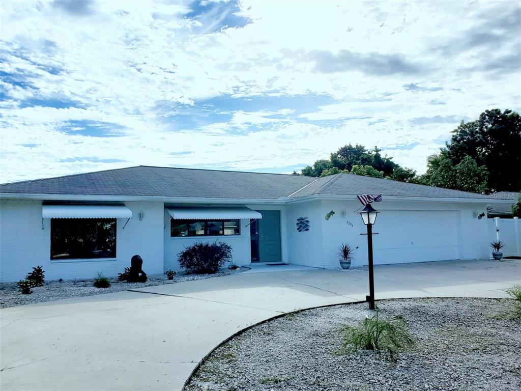A white, single-story ranch-style house features a large driveway, a two-car garage, and metal awnings — 2203 43RD STREET W, BRADENTON, FL