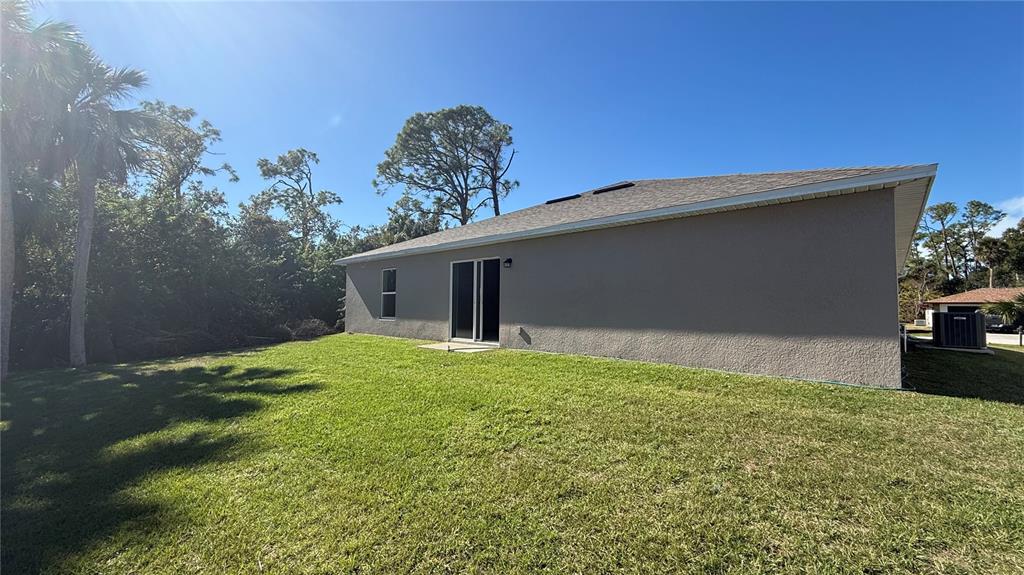 The exterior of a single-story house features a gray stucco wall, a sliding glass door, and a grassy yard — 2168 CLERMONT STREET, PORT CHARLOTTE, FL