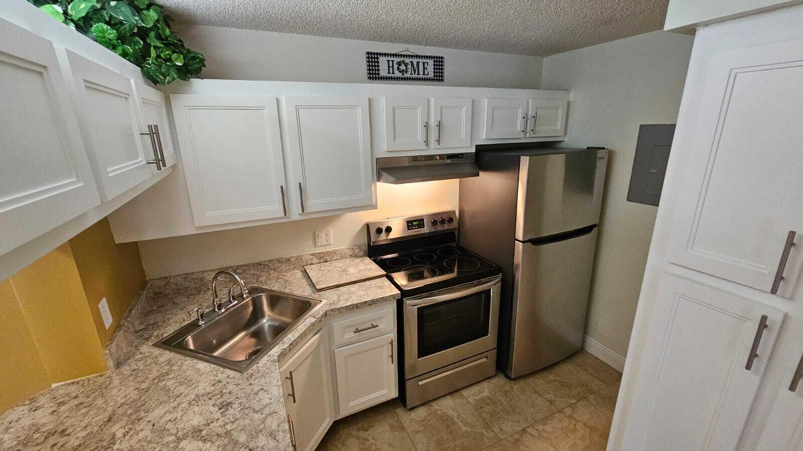 A kitchen features white cabinets, stainless steel appliances, and granite-look countertops — 205 Foxtail Drive # H3, FL 33415, FL