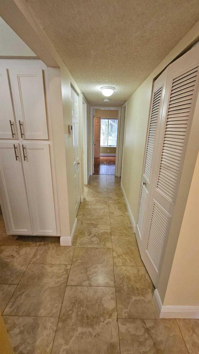 A hallway with beige tile flooring, white cabinetry, and louvered closet doors leads to another room — 205 Foxtail Drive # H3, FL 33415, FL