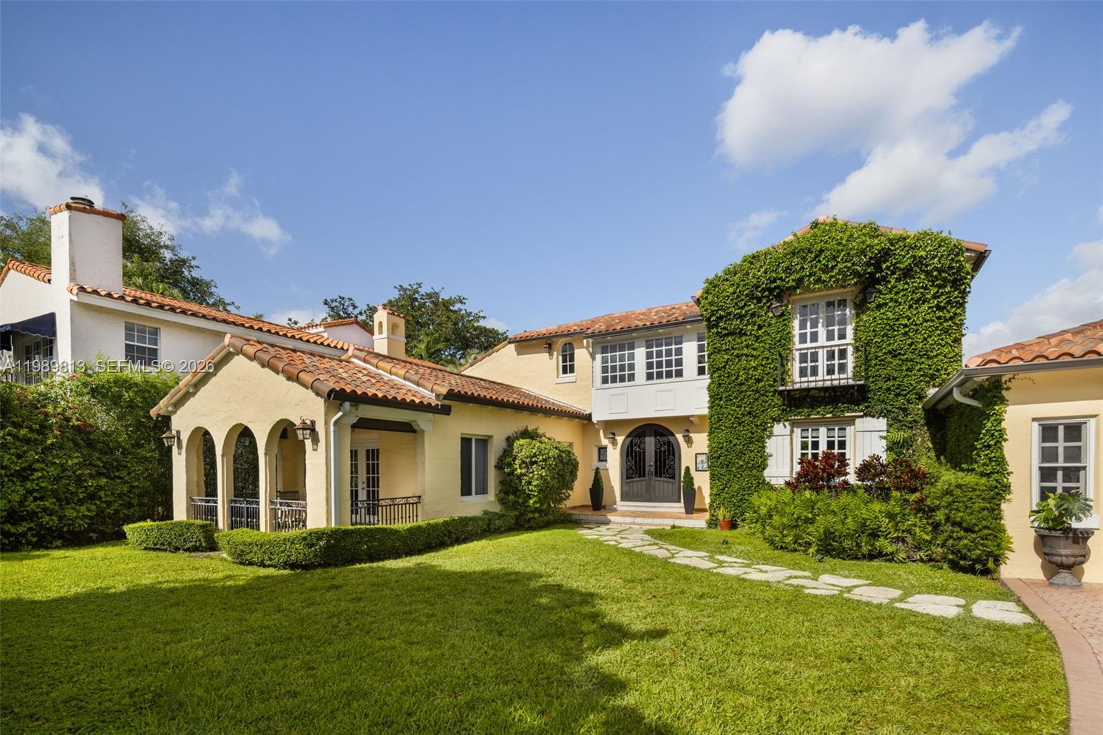 A two-story Mediterranean-style house features a vine-covered exterior, a tiled roof, and a stone walkway — 4206 Alhambra Cir, Coral Gables FL 33146, CORAL GABLES, FL