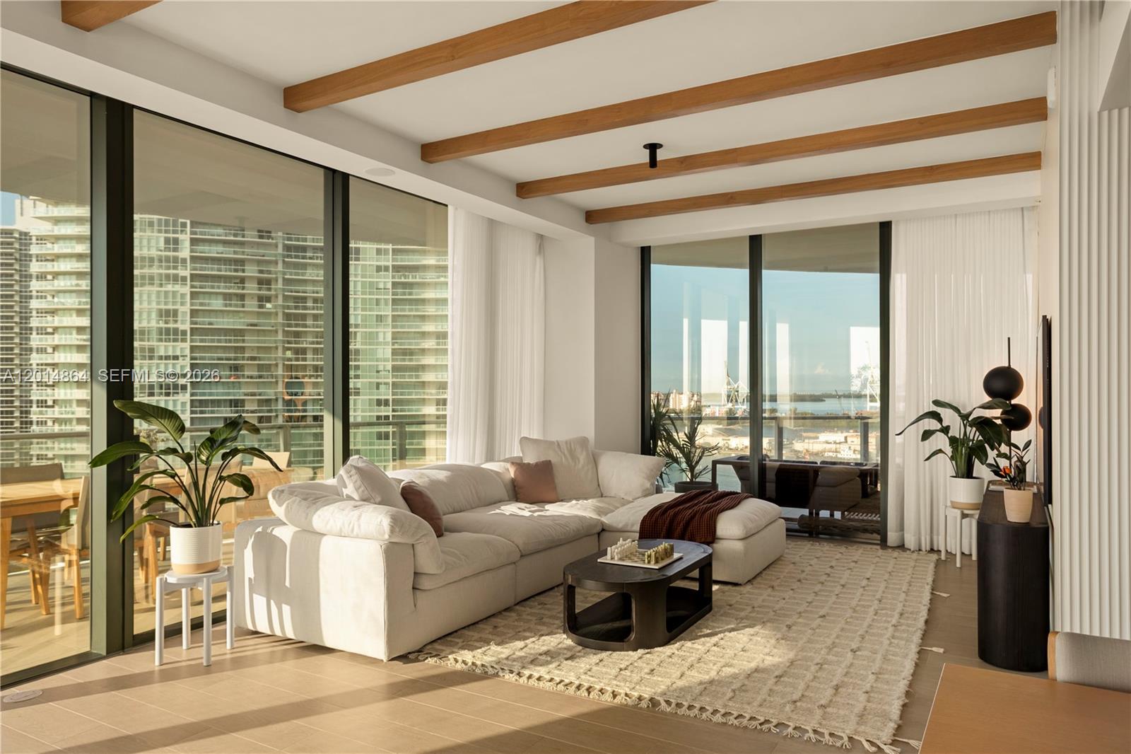 A modern living room features wood ceiling beams, a white sectional sofa, and floor-to-ceiling windows — 500 Alton Rd # 1601, Miami Beach FL 33139, MIAMI BEACH, FL